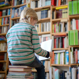 Ein Kind sitzt auf einem Buchstapel und liest ein Buch © imago/Thomas Eisenhuth