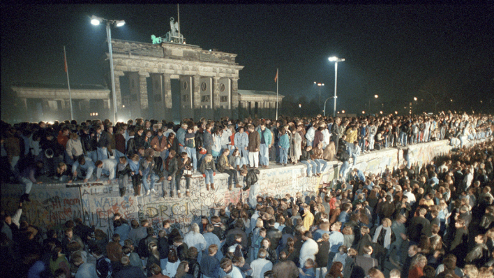 Menschen auf der Berliner Mauer vor dem Brandenburger Tor in der Nacht vom 9. auf den 10.11.1989 © picture alliance/dpa | Peter Kneffel