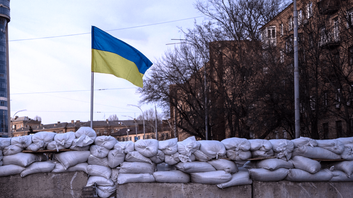 Eine ukrainische Flagge weht vor einer Barrikade in Kyjiw © picture alliance / ASSOCIATED PRESS | Rodrigo Abd