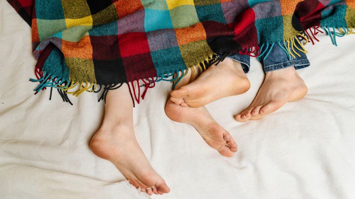 Füße eines Paares schauen unter einer Decke hervor © IMAGO / Westend61