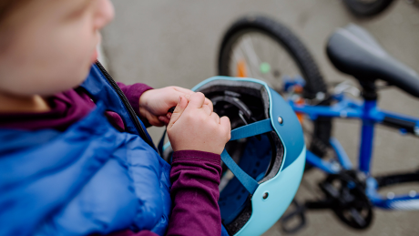 Ein Kind steht mit einem Helm in der Hand neben einem Fahrrad © IMAGO / HalfPoint Images