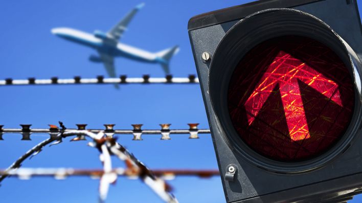 Stacheldraht und rotes Ampellicht vor startendem Flugzeug © IMAGO / Christian Ohde