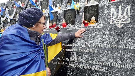 Eine Frau mit ukrainischer Flagge berührt am 21.11.2024 ein Denkmal für gefallene Soldaten © imago images/Avalon.red