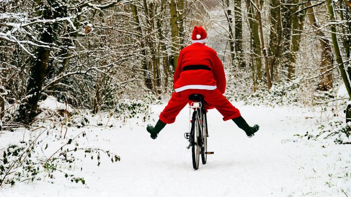 Ein als Weihnachtsmann verkleideter Radfahrer fährt durch einen verschneiten Wald © imago images/Ardea