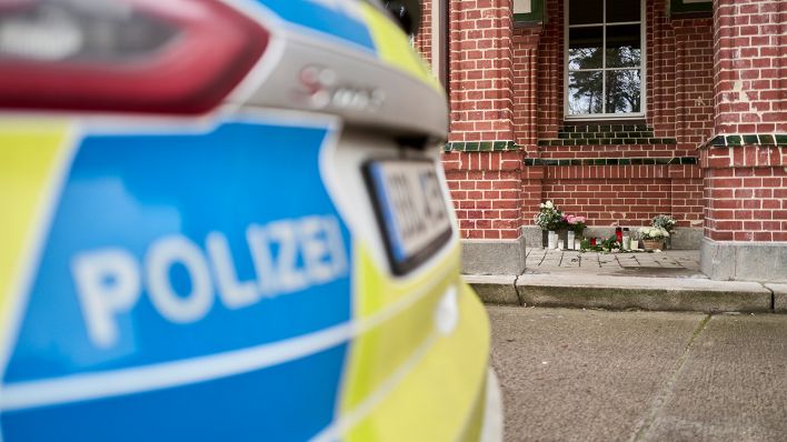 Beelitz: Blumen und Kerzen stehen vor dem Eingang eines Hauses nach einem Gewaltverbrechen vor dem ein Polizeifahrzeug steht © Michael Ukas/dpa