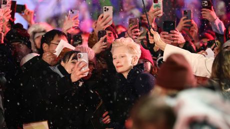 Schauspielerin Tilda Swinton steht am Eröffnungsabend der Berlinale auf dem Roten Teppich mit Zuschauern zusammen © Christoph Soeder/dpa